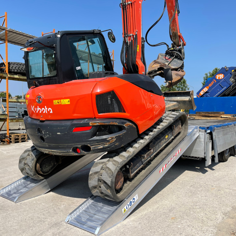 Ein Bagger wird mithilfe der Schwerlast Auffahrrampen M230 auf eine Ladefläche verladen, die Ansicht ist von schräg hinten